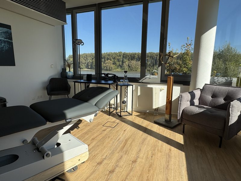 Therapieraum mit Behandlungsliege, Sessel und Panoramafenstern
