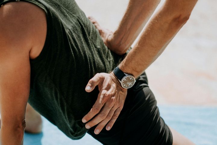 Therapeut behandelt mit beiden Händen den unteren Rücken eines auf dem Bauch liegenden Mannes