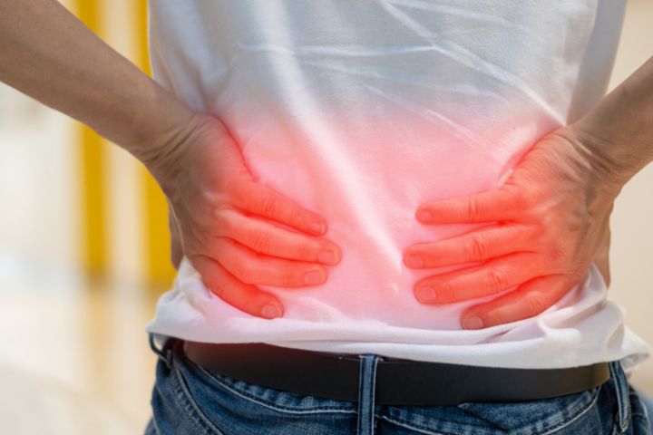 Person hält sich mit beiden Händen den unteren Rücken, die Stelle ist rot hervorgehoben