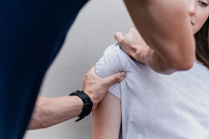 Therapeut untersucht mit beiden Händen die Schulter einer Patientin